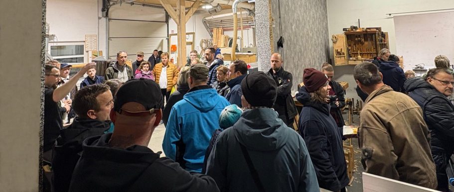 Gruppendiskussion in einer Werkstatt mit mehreren Personen und Werkzeugen im Hintergrund.